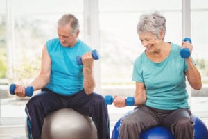 Senior man and woman sitting on exercise balls while lifting weights