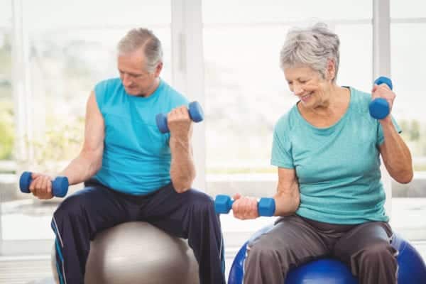 Senior man and woman sitting on exercise balls while lifting weights