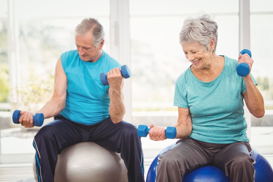 Senior man and woman sitting on exercise balls while lifting weights