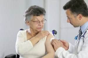 an elderly woman is preparing to receive a vaccine shot from a doctor
