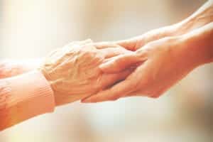 Senior woman’s hands being held by younger woman’s hands.