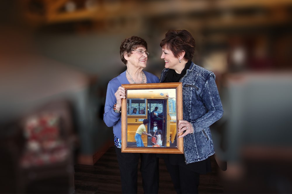 A mother and daughter stand together holding a photograph.