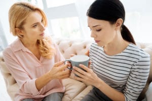 Woman comforting and handing cup of coffee to distressed friend.