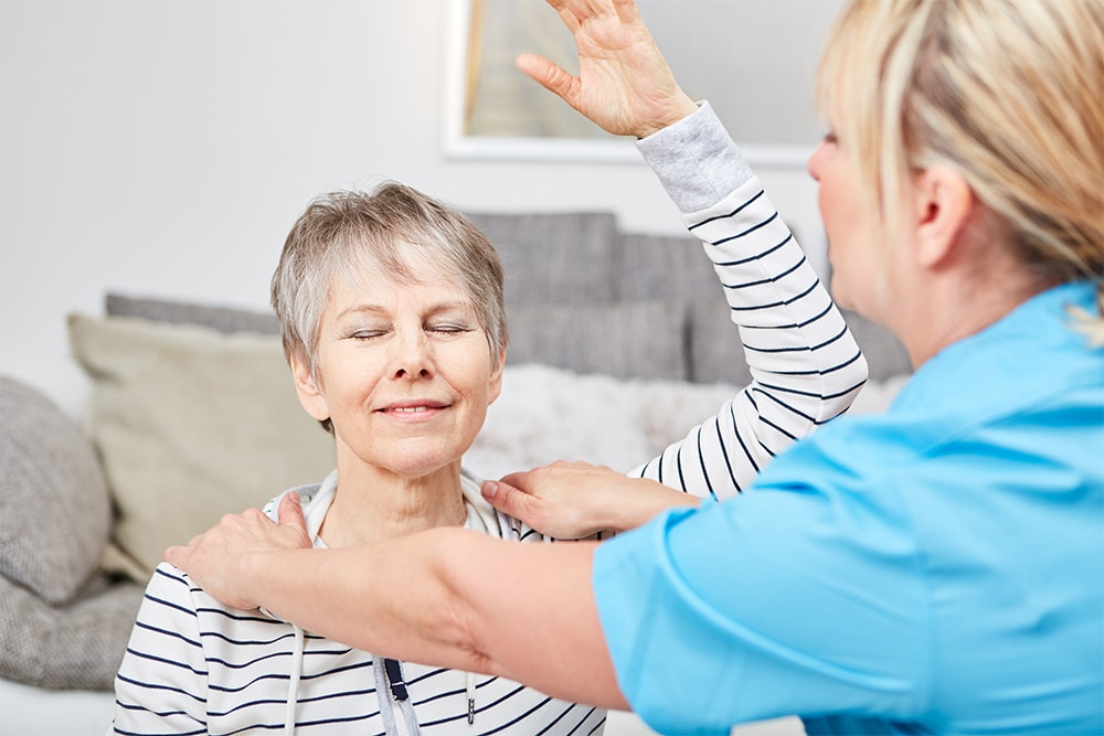 Woman smiling while she lifts arm above her head and physical therapist holds down shoulders.