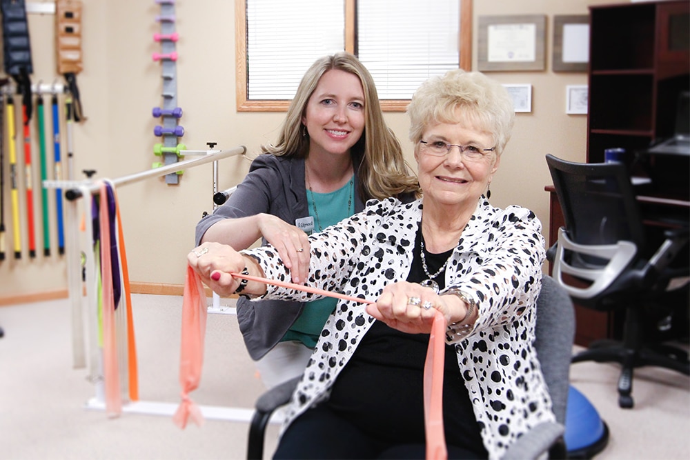 Senior woman pulls on therapy band while physical therapist smiles.