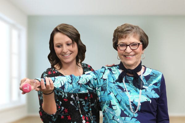 Physical therapist helping senior woman lift a weight.