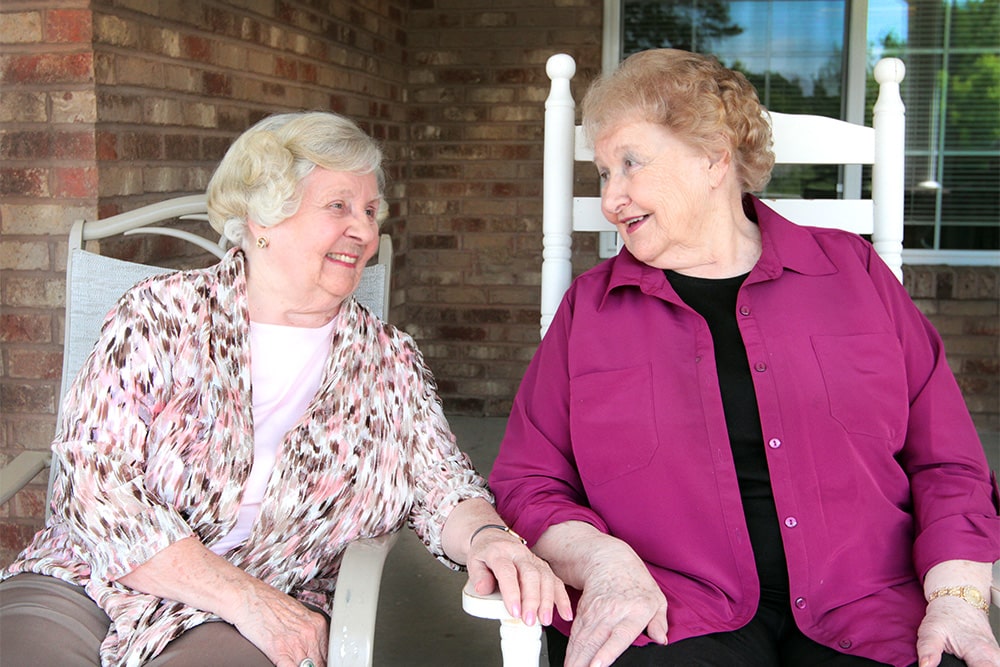 Two elderly women chatting on a porch.