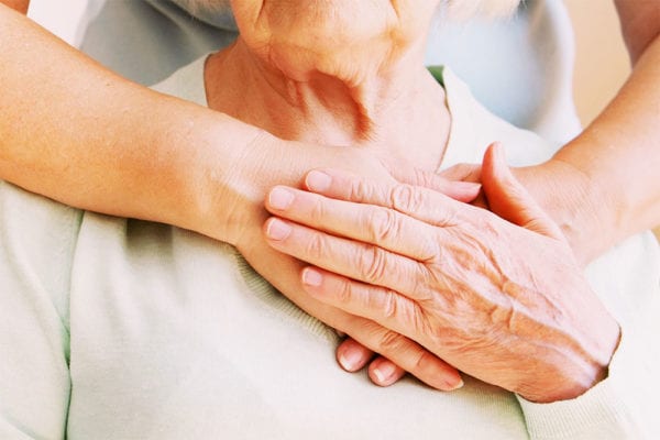 Senior woman touching the the hand of the person whose arms are wrapped around her.