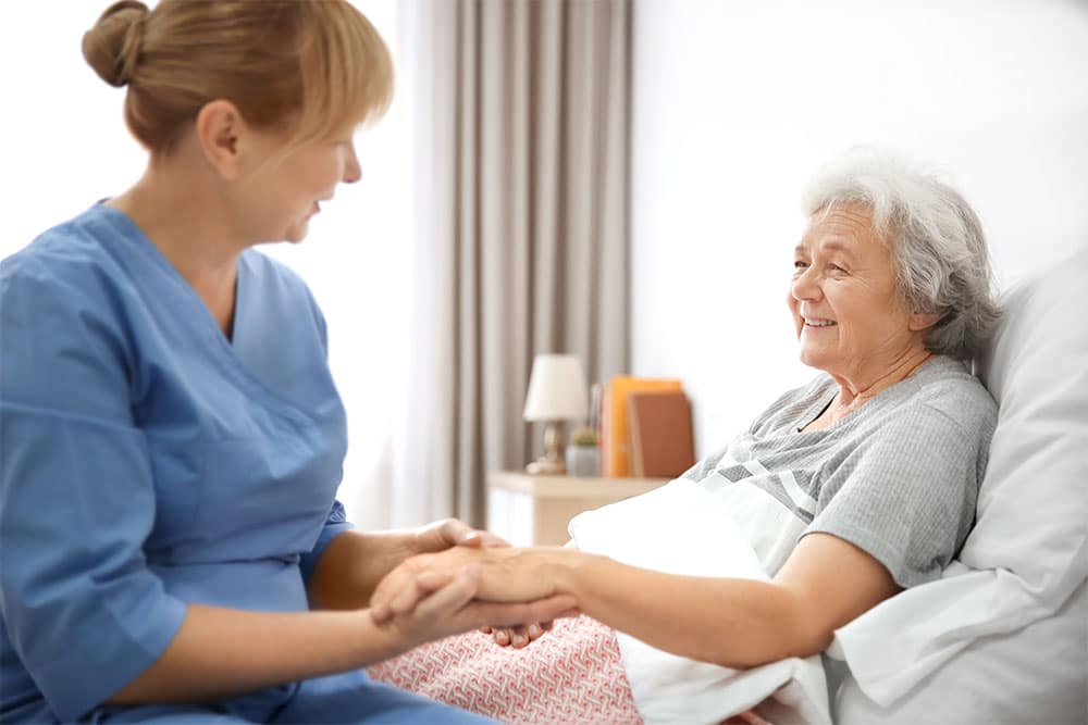 Nurse smiles and talks to senior woman in hospital bed.