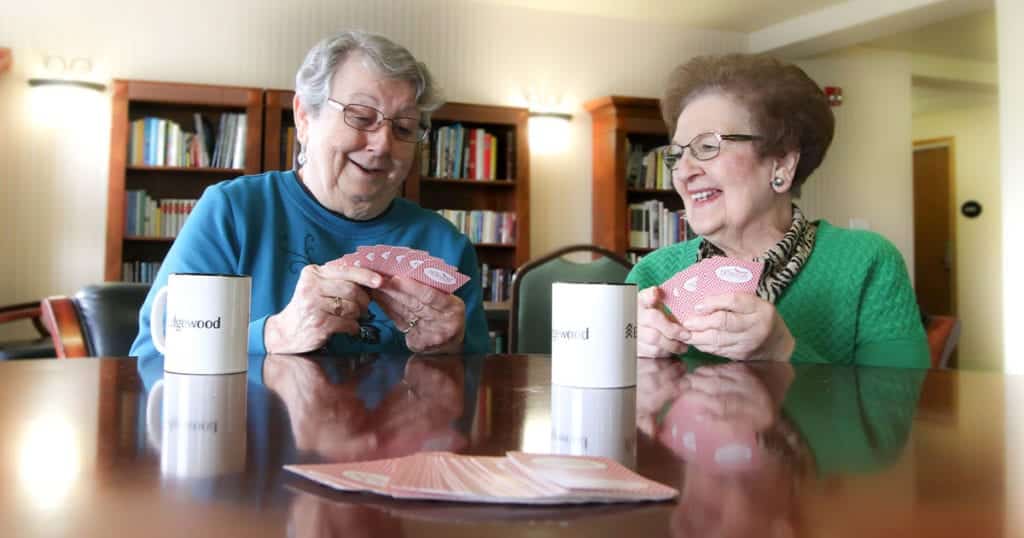 Two senior women smile as they play cards together
