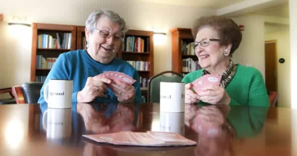 Two senior women smile as they play cards together