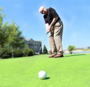 A senior man putts a golf ball on a bright, sunny golf course