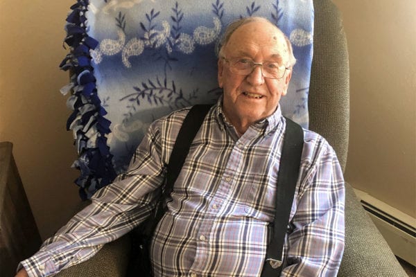 A portrait of Edgewood Healthcare resident Harold Weidler smiling at the camera as he sits in a green recliner