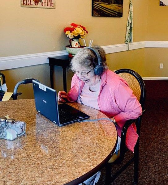 A senior woman smiling at a laptop while sitting at a table during a telehealth appointment