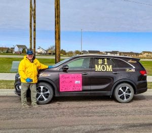 Tim Flakoll smiles as he stands on a road next to his SUV, which is decorated with messages to his mom for the Mother’s Day car parade at Edgewood Healthcare