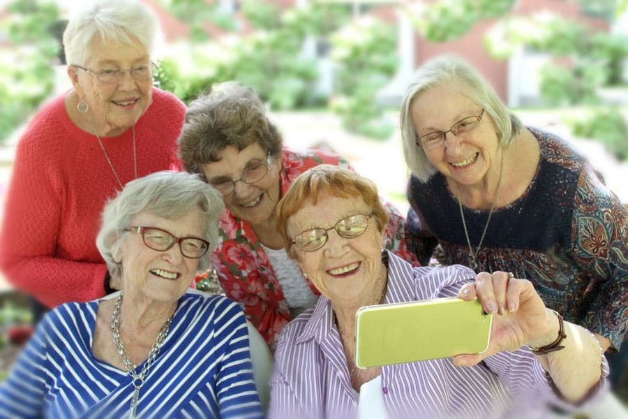 A group of five cheerful senior women smile as they pose for a selfie.