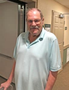 Edgewood resident Dave Bryant smiles for the camera while taking a stroll with his walker in the hallway of his home community.