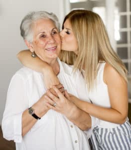 A young woman hugging a senior woman while kissing her cheek