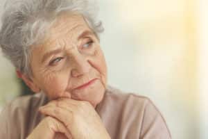 A senior woman looks off into the distance while resting her head on her hands