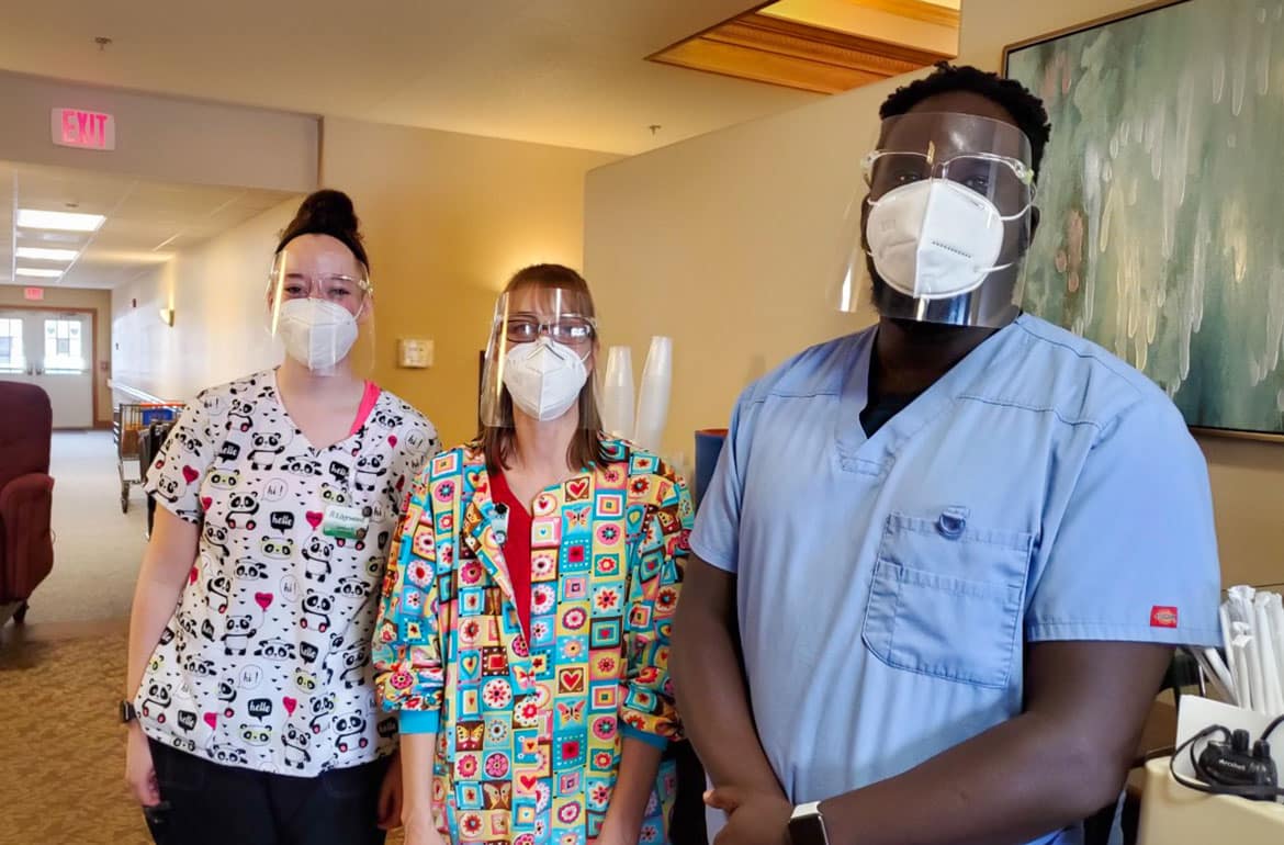 Three Edgewood employees, two female and one male, wearing scrubs and personal protective equipment stand next to one another to pose for a photo.