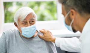 A senior man wearing a mask smiles at a male doctor sitting in front of him.