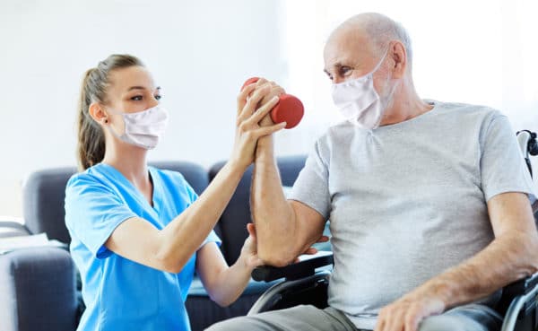 A young female nurse helps a senior man lift a free weight during a physical therapy appointment