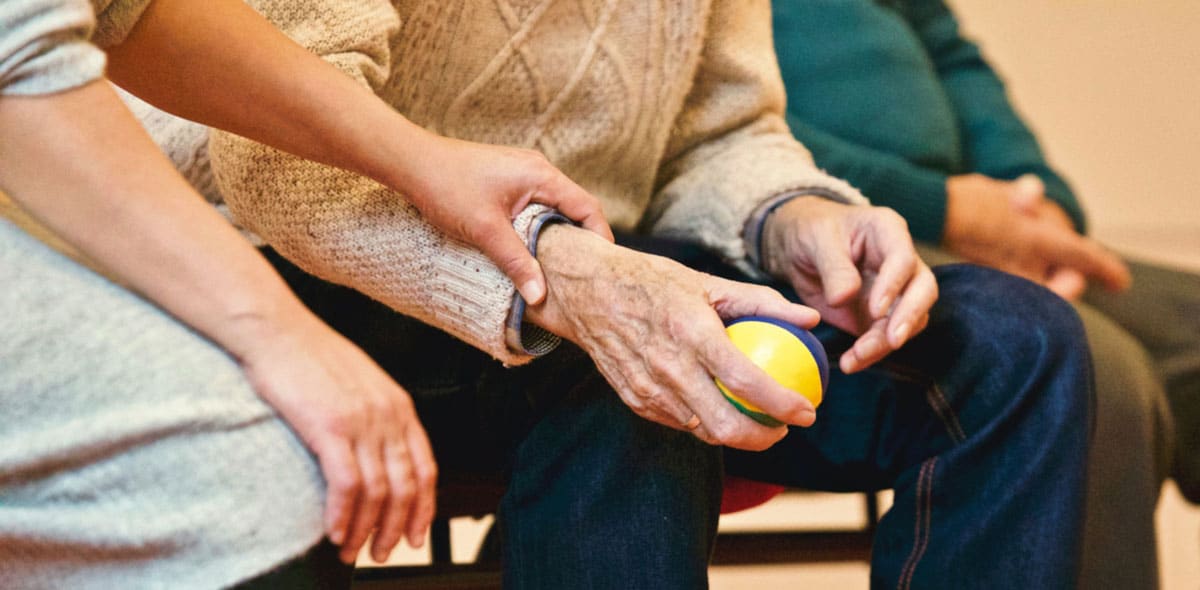 Elder man doing hand movements with a therapy ball.
