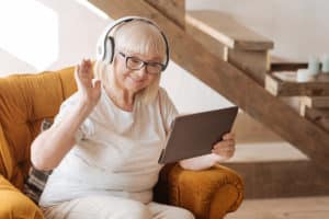 Female senior wearing white headphones waving at tablet screen