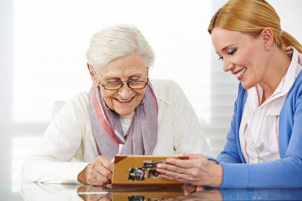 female senior in white and female loved one in blue looking at memory book photo