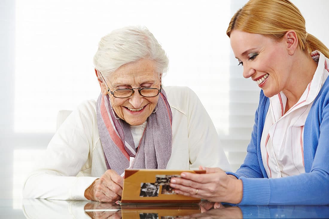 female senior in white and female loved one in blue looking at memory book photo