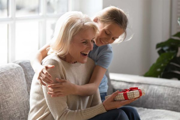 Senior Female receiving a gift from female child who’s embracing her