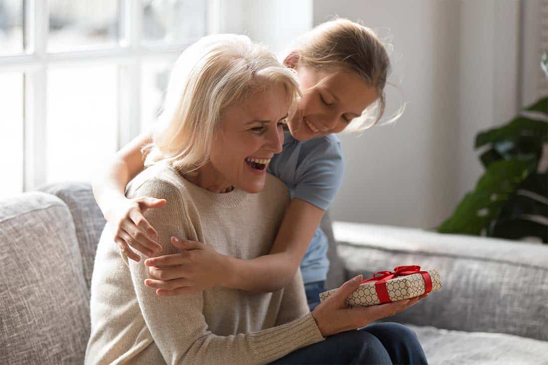 Senior Female receiving a gift from female child who’s embracing her