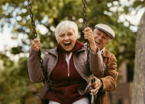 female senior wearing a purple jacket being pushed on swing by male senior wearing a brown jacket and hat