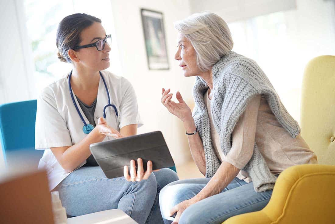 image of female clinician with tablet next to female senior with sweater around neck