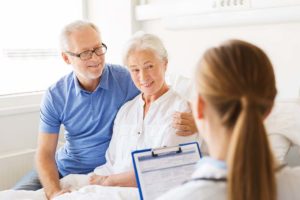 Senior male wearing a blue polo female senior wearing a white button down with a female clinician holding clipboard