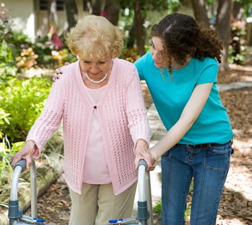 Senior female walking with walker next to young woman