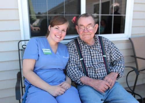 Female staff wearing blue scrubs with male senior seated outdoors