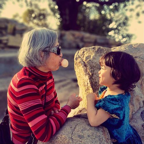 Female senior blowing a bubble with bubble gum next to a child
