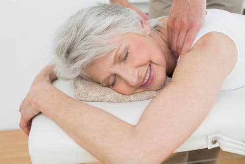 Senior female lying in prone position receiving a neck massage