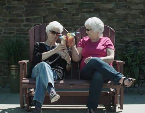 Female seniors seated on bench holding drinks with umbrellas