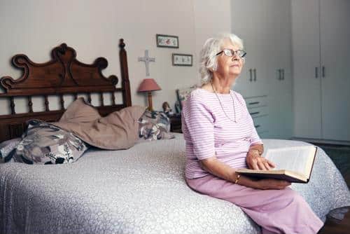 Senior female seated on bed with book