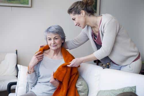 Female putting shawl around neck of female senior