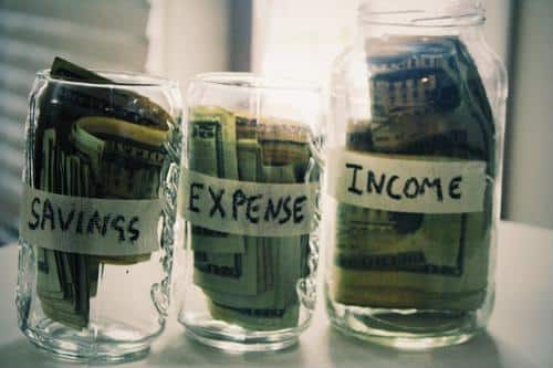 Money in glass jars labled savings, expenses, and income