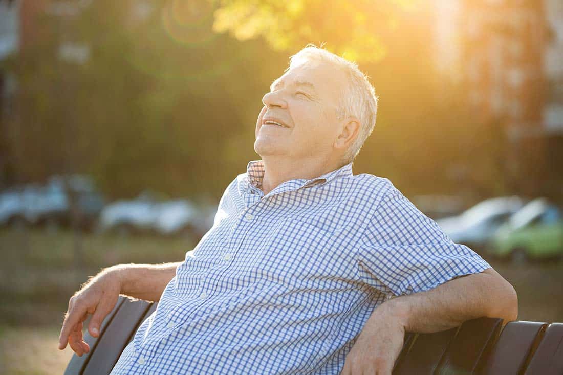 Senior male seated on bench with sun in the distance