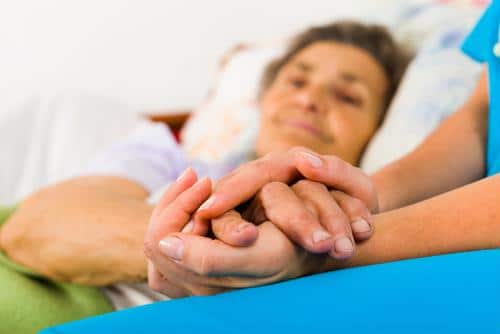 Clinical staff wearing blue scrubs holding hands of patient lying in bed