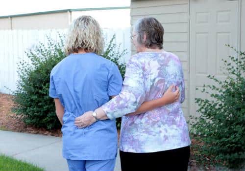 Caregiver and female senior walking away from camera