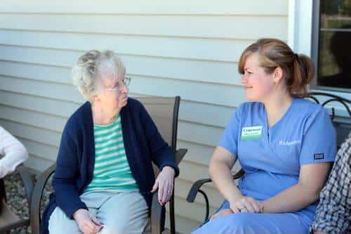 Female resident seated outside next to female staff wearing blue scrubs