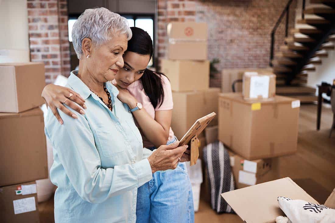 Senior female looking at photo frame with female embracing her
