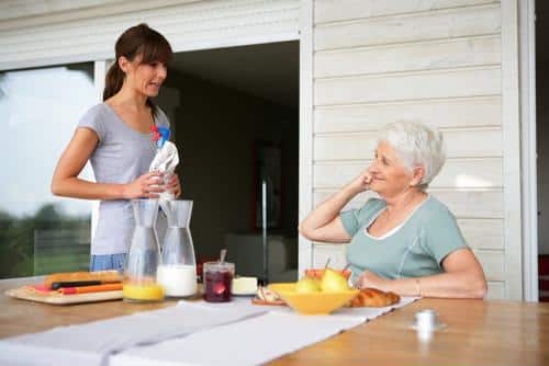 Female senior seated at table speaking to young woman