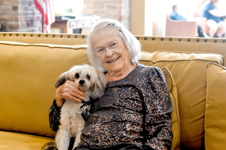 senior female wearing a sparkly shirt pictured on couch with her dog